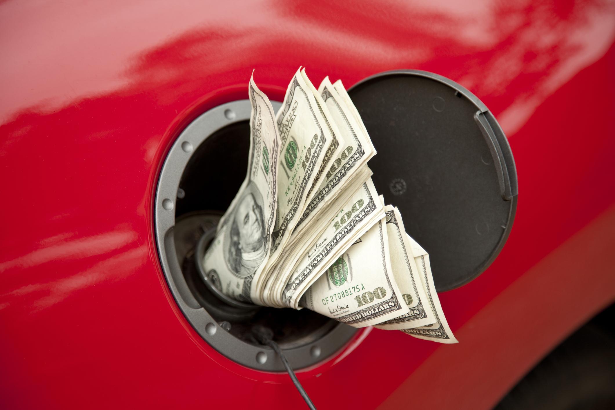 Concept shot of hundreds of dollars going into the gas tank of a red vehicle.  Price of gas continues to go higher.